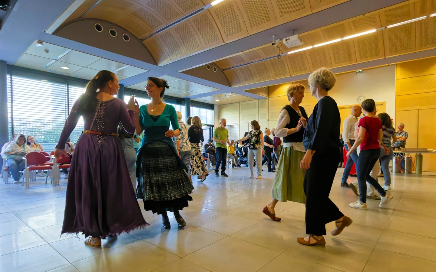People in traditional dresses dance together in a community hall.