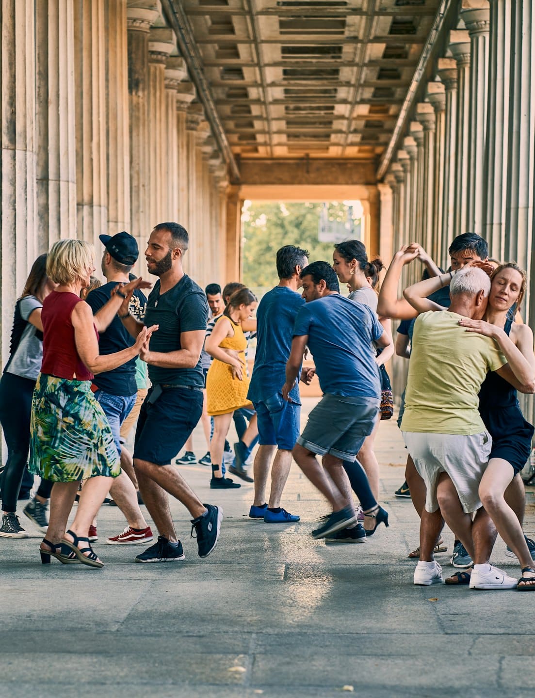 Adults dancing salsa under a stone colonnade.