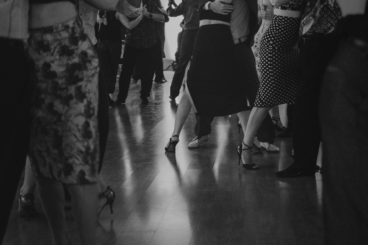 Couples dance on a polished wooden floor in elegant attire.